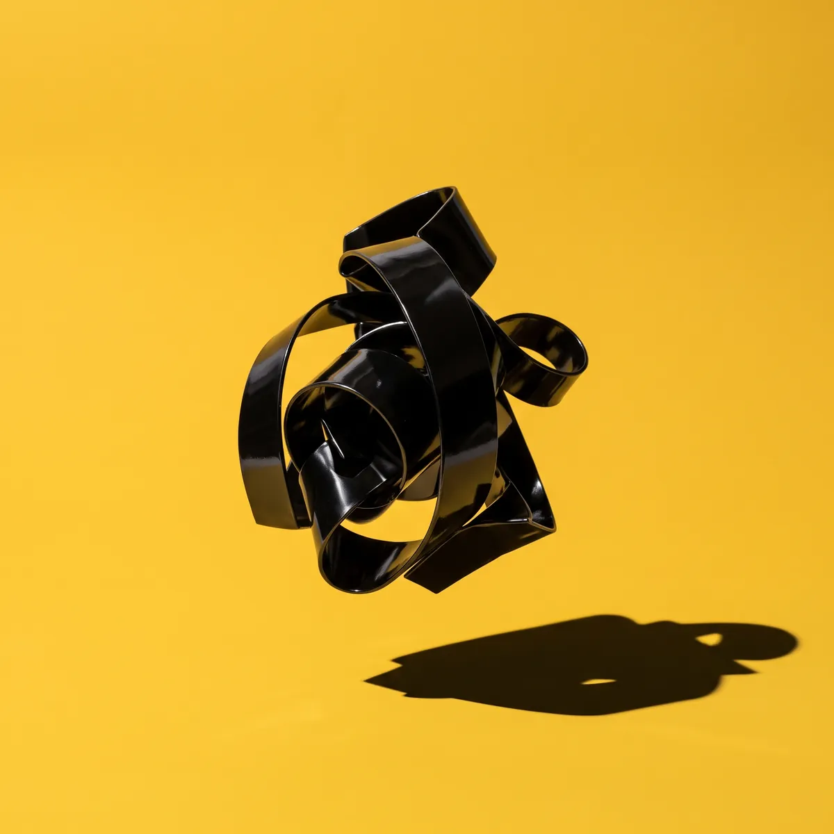 Glossy black folded-metal sculpture floating over NZ Marketing yellow, brand campaign art